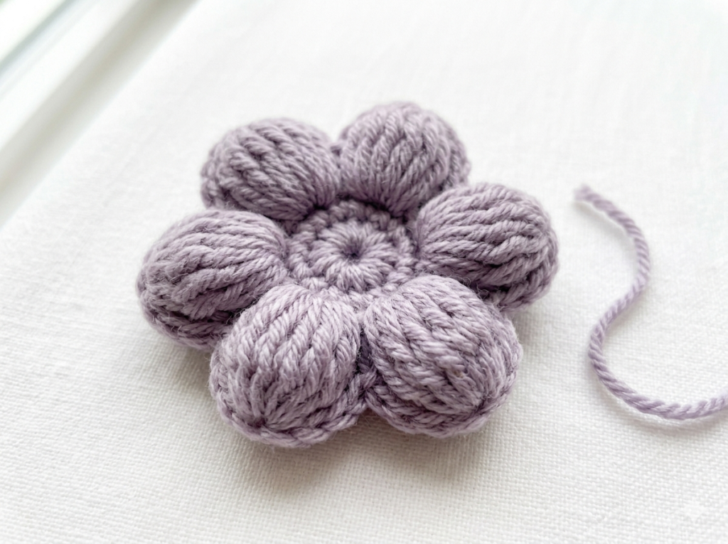 finished puff stitch tiny crochet flower in lavender yarn with plump rounded 3D petals on white surface